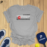 Gray t-shirt with 'Picklelegenes' design on a wooden surface with pickleball equipment.