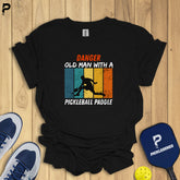 Black t-shirt with pickleball-themed design on a wooden surface with pickleball equipment.