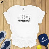 White t-shirt with 'PICKELEGNES' design on a wooden surface with pickleball equipment.