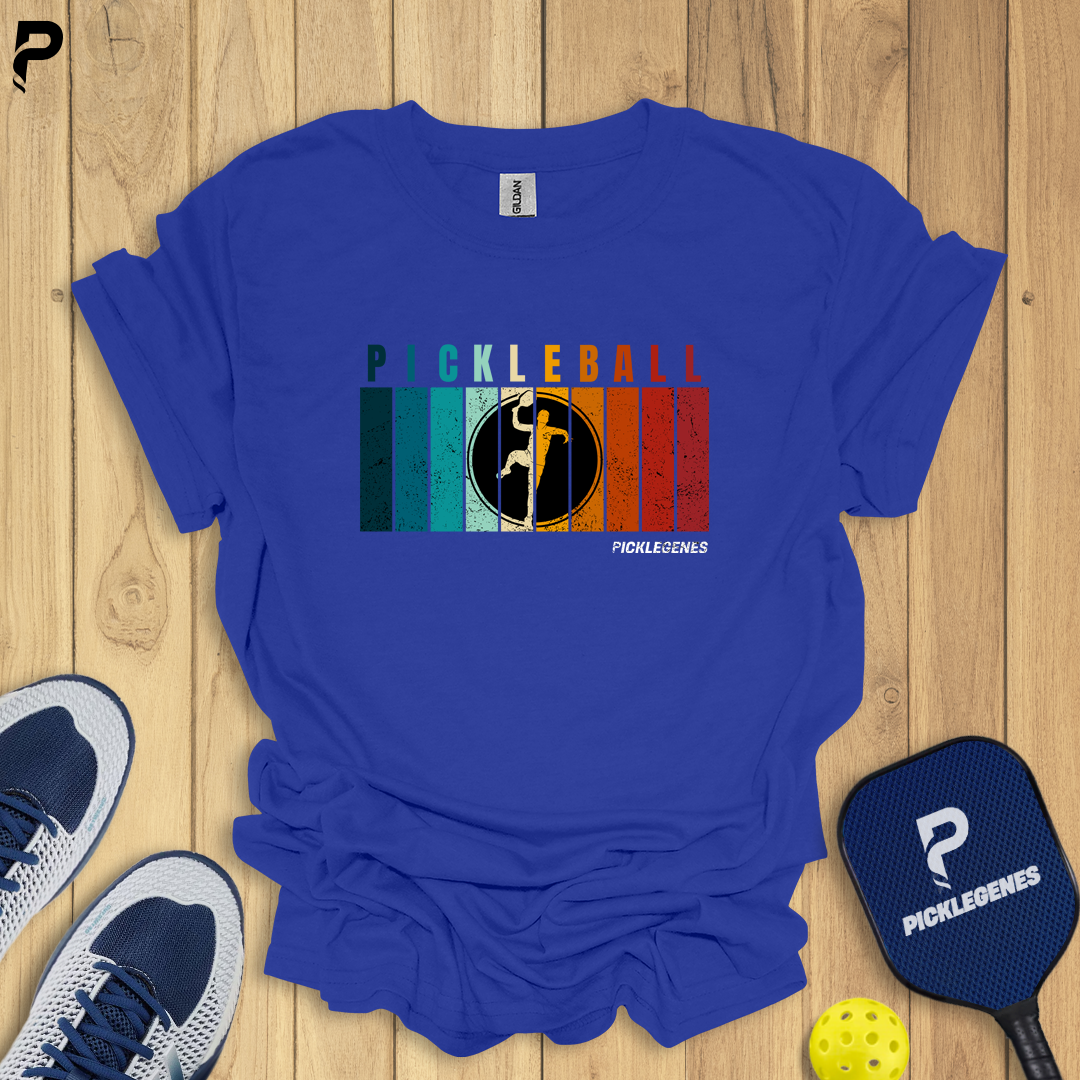 Blue t-shirt with pickleball design on a wooden surface with shoes and paddle.