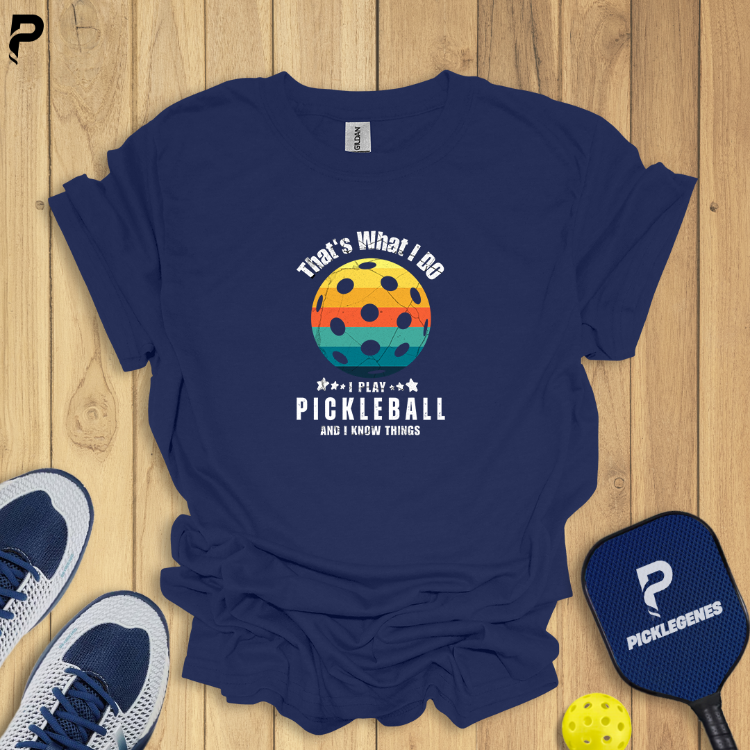 Navy blue t-shirt with pickleball design on a wooden surface with shoes and paddle.