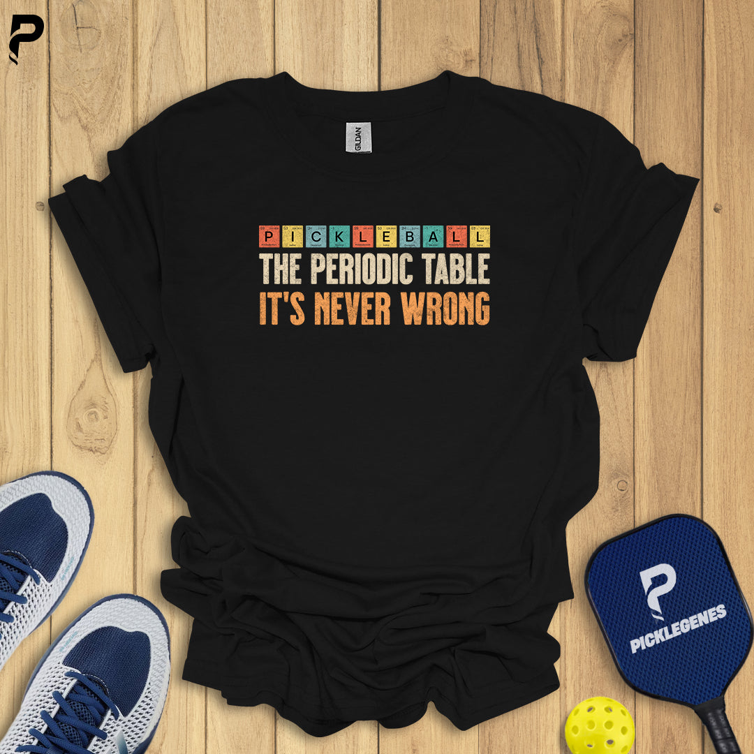 Black t-shirt with colorful text on a wooden surface with pickleball equipment.