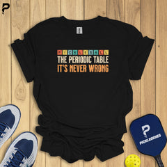 Black t-shirt with colorful text on a wooden surface with pickleball equipment.