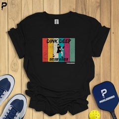 Black t-shirt with colorful graphic design on a wooden surface with sports equipment.
